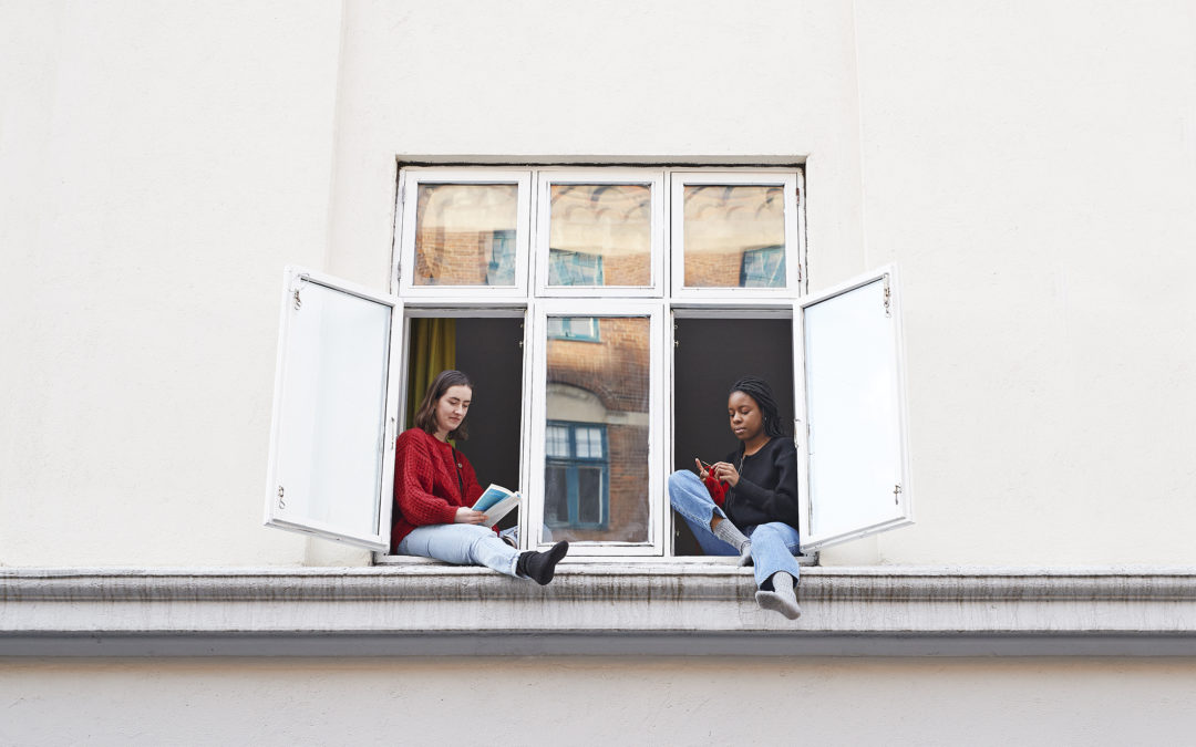 Young women reading and knitting in apartment window during COVID-19 isolation
