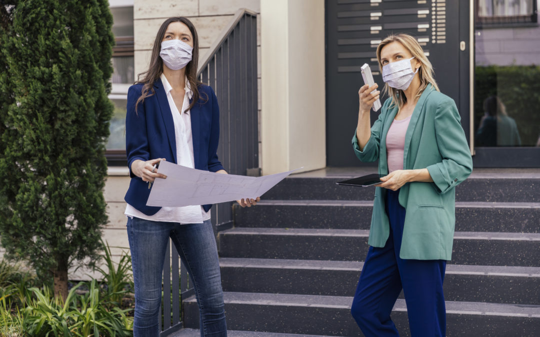 Real estate agent and client wearing face masks while inspection outdoor area of houses