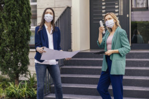 Real estate agent and client wearing face masks while inspection outdoor area of houses
