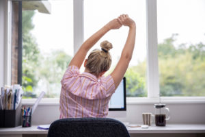 Rear view of woman working on computer in office stretching at desk