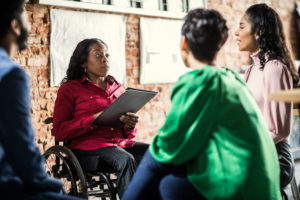 Black businesswoman in wheelchair leading group discussion with three other people in an office